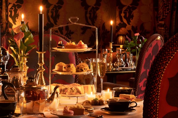 Rhurbarb Edinburgh restaurant table set for afternoon tea with a three-tier stand of pastries, scones, and sandwiches, teapot, teacups, champagne glasses, candles, and flowers