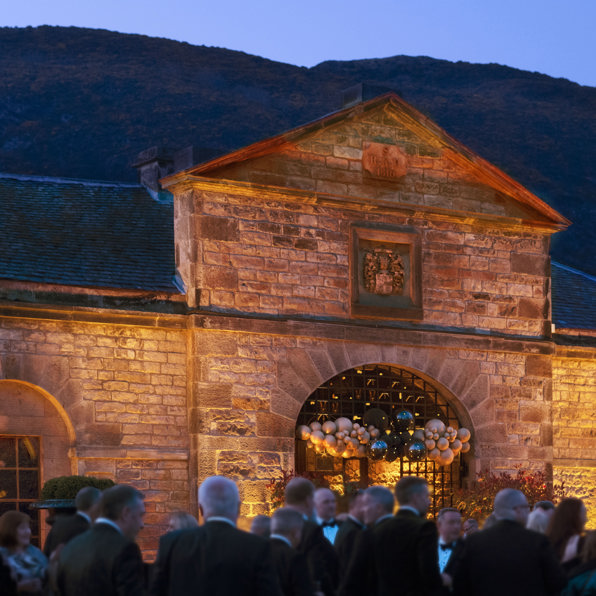 Guests dressed in black tie attire outside The Stables venue in Edinburgh at evening event drinks reception on the lawn at Prestonfield